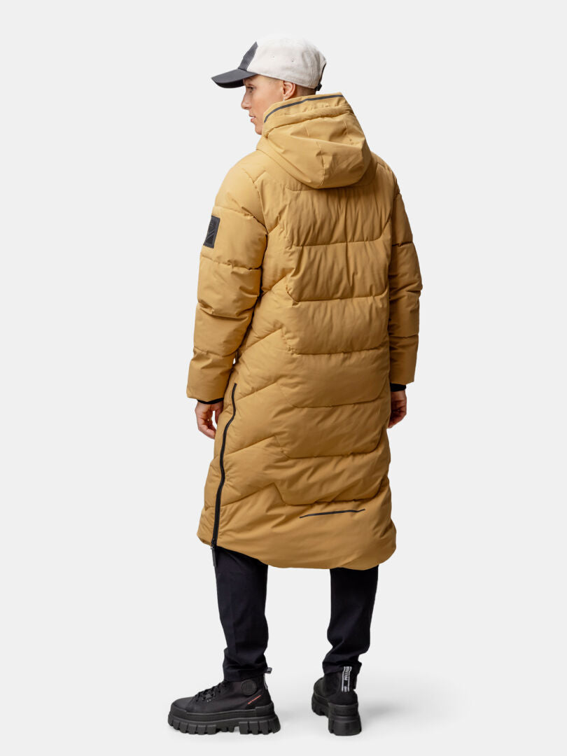 Person, die eine Halti Brahe Puffer Long Winterjacke Damen, eine schwarze Hose, schwarze Schuhe und eine hellgraue Mütze trägt, mit Blickrichtung nach außen.