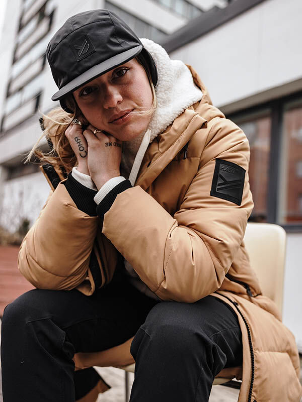 Frau trägt Halti Brahe Puffer Long Winterjacke und sitzt nachdenklich draußen, das Gesicht berührend.