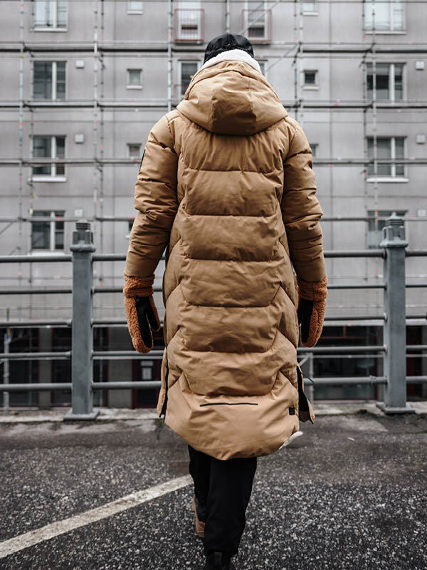 Frau trägt Halti Brahe Puffer Long Winterjacke aus recyceltem Polyester, läuft vor Stadtkulisse.