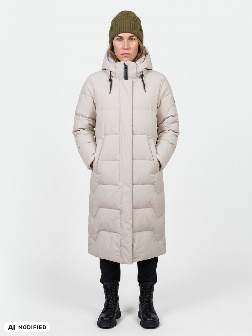 Eine Person blickt nach vorne und trägt eine „Halti Brahe Puffer Long Winterjacke Damen“, eine grüne Mütze, eine schwarze Hose und Stiefel.