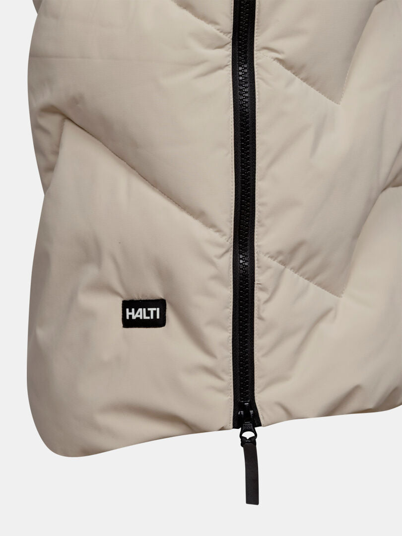 Nahaufnahme der „Halti Brahe Puffer Long Winterjacke“ für Damen in Beige mit DrymaxX, schwarzem Reißverschluss und Logo-Aufnäher.