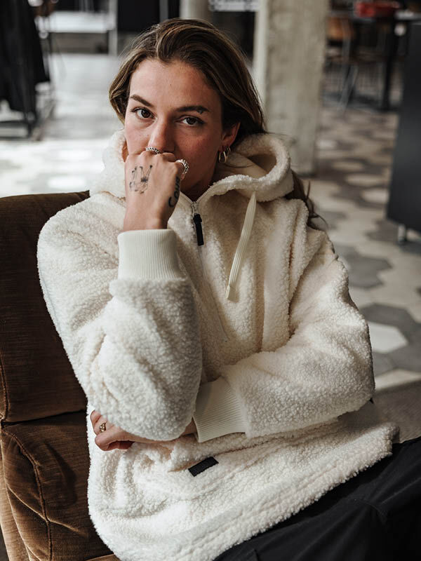 Eine Frau in einer Halti Lykky Fleece Jacke Damen aus recyceltem Polyester sitzt in einem Haus und blickt in die Kamera.