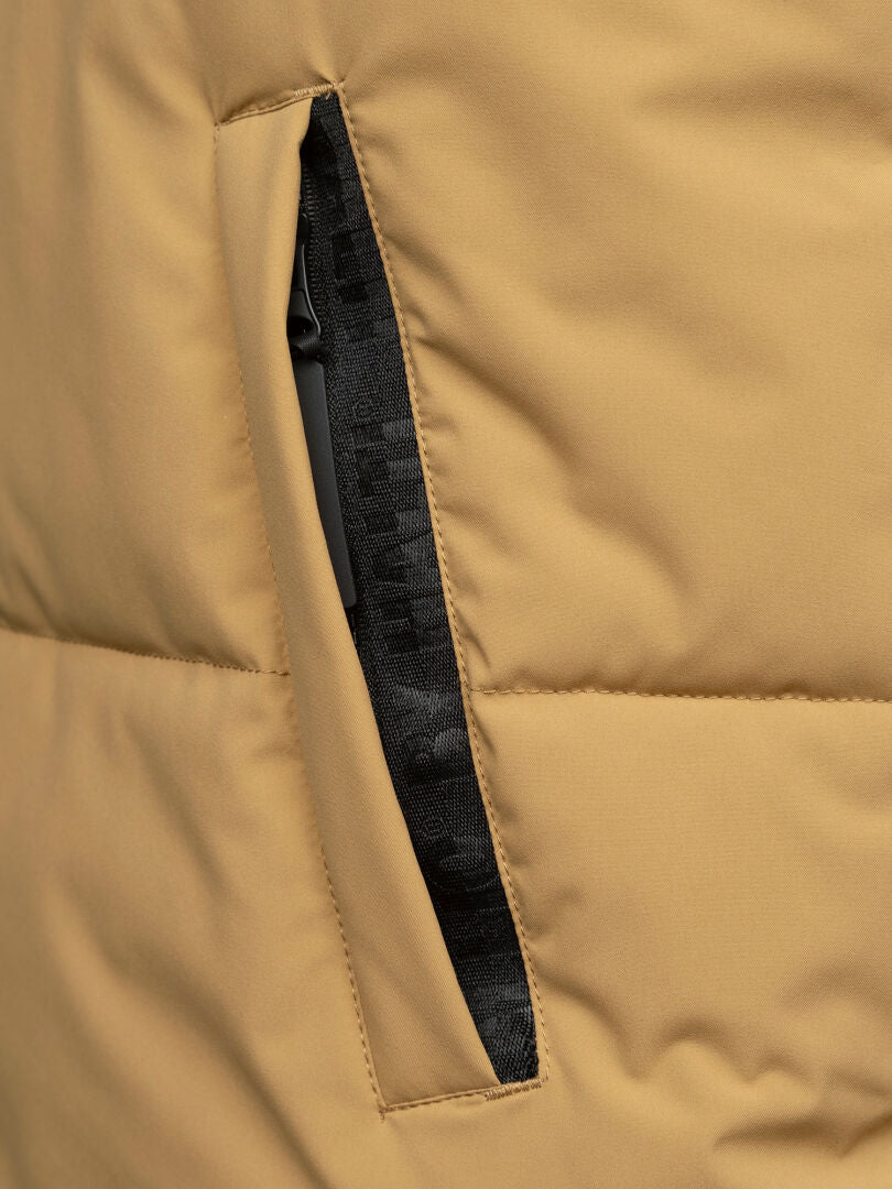 Nahaufnahme einer hellbraunen Halti Penger Classic Puffer Weste Herren mit einem teilweise offenen schwarzen Reißverschluss an der Seitentasche.