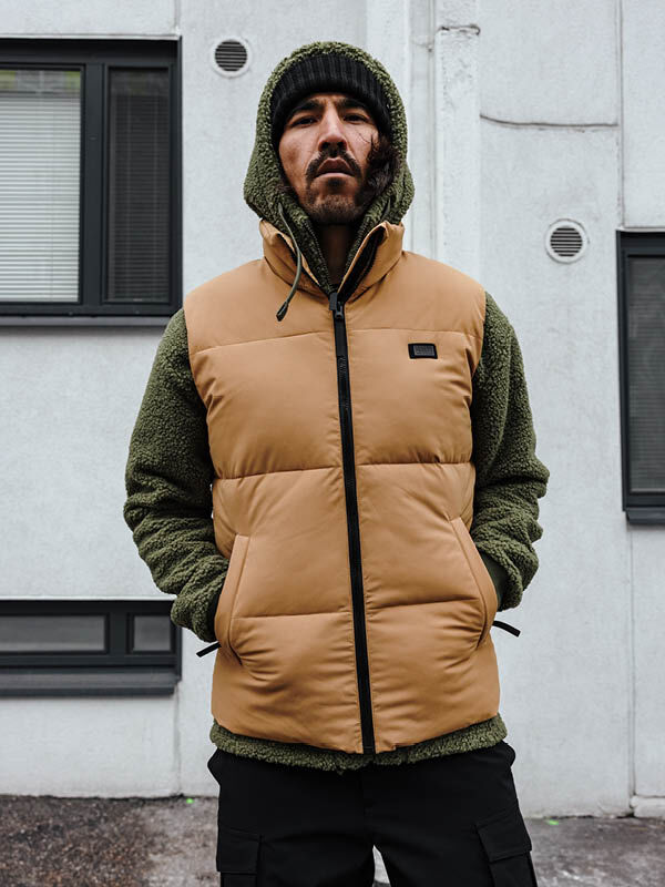 Ein Mann in einer Halti Penger Classic Puffer Weste Herren steht vor einem hellgrauen Gebäude mit Fenstern.