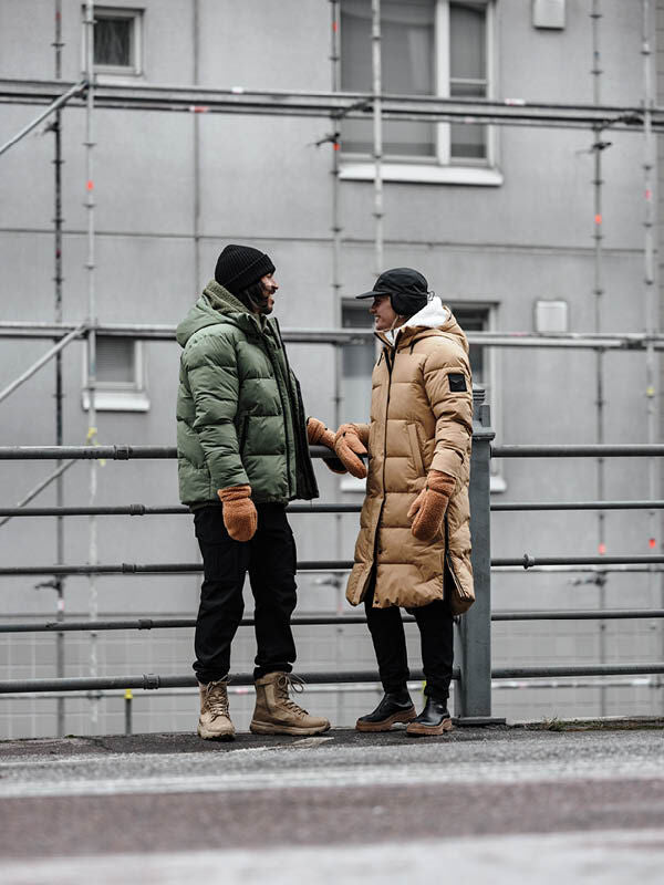 Zwei Personen in Halti Brahe Puffer Long Winterjacke Damen unterhalten sich in der Nähe eines Geländers und Gerüsts.