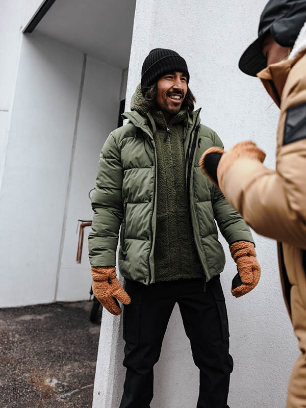 Zwei Männer in Halti Brahe Puffer Winterjacke Herren mit Zweischicht-Isolierung plaudern und lächeln an einer weißen Wand.