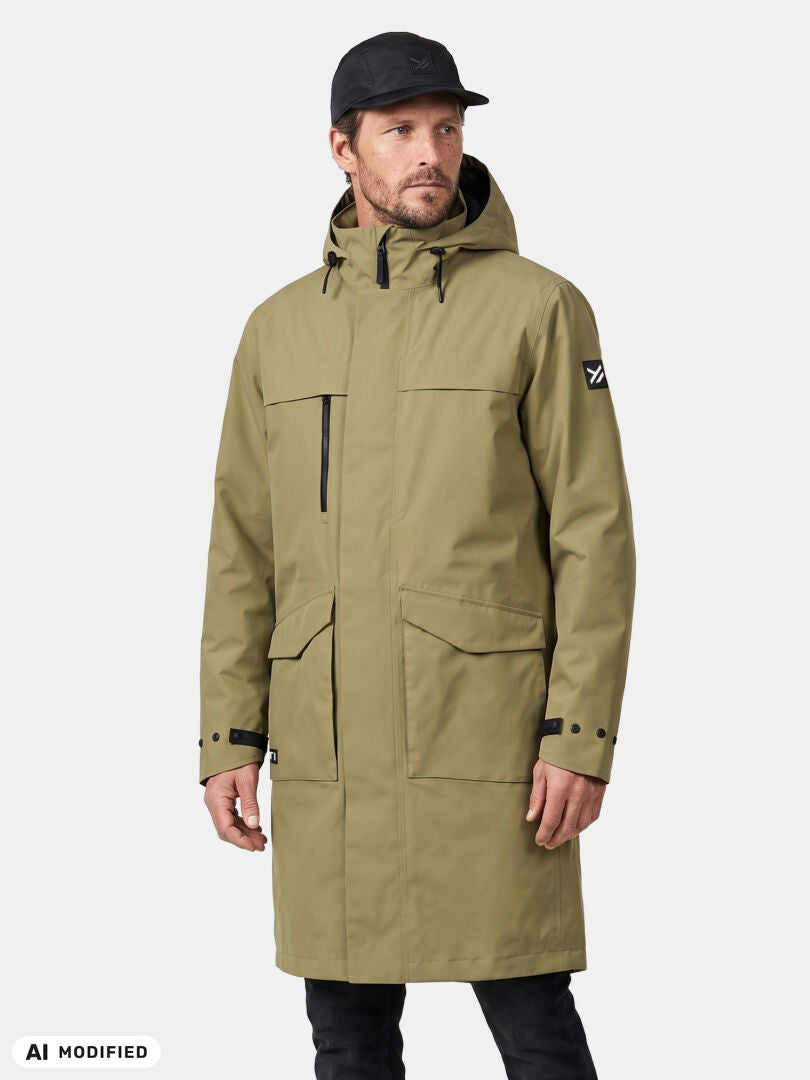 Ein Mann in einer „Halti Tokoi II DX Parka“-Jacke für Herren und einer schwarzen Mütze steht vor einem einfarbigen Hintergrund und blickt leicht nach rechts.