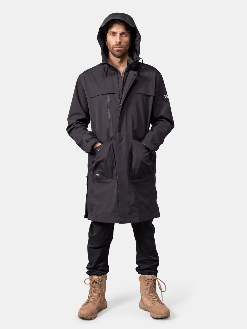 Ein Mann in einer „Halti Tokoi II DX Parka“-Jacke, einer schwarzen Hose und hellbraunen Stiefeln steht vor einem einfarbigen Hintergrund.