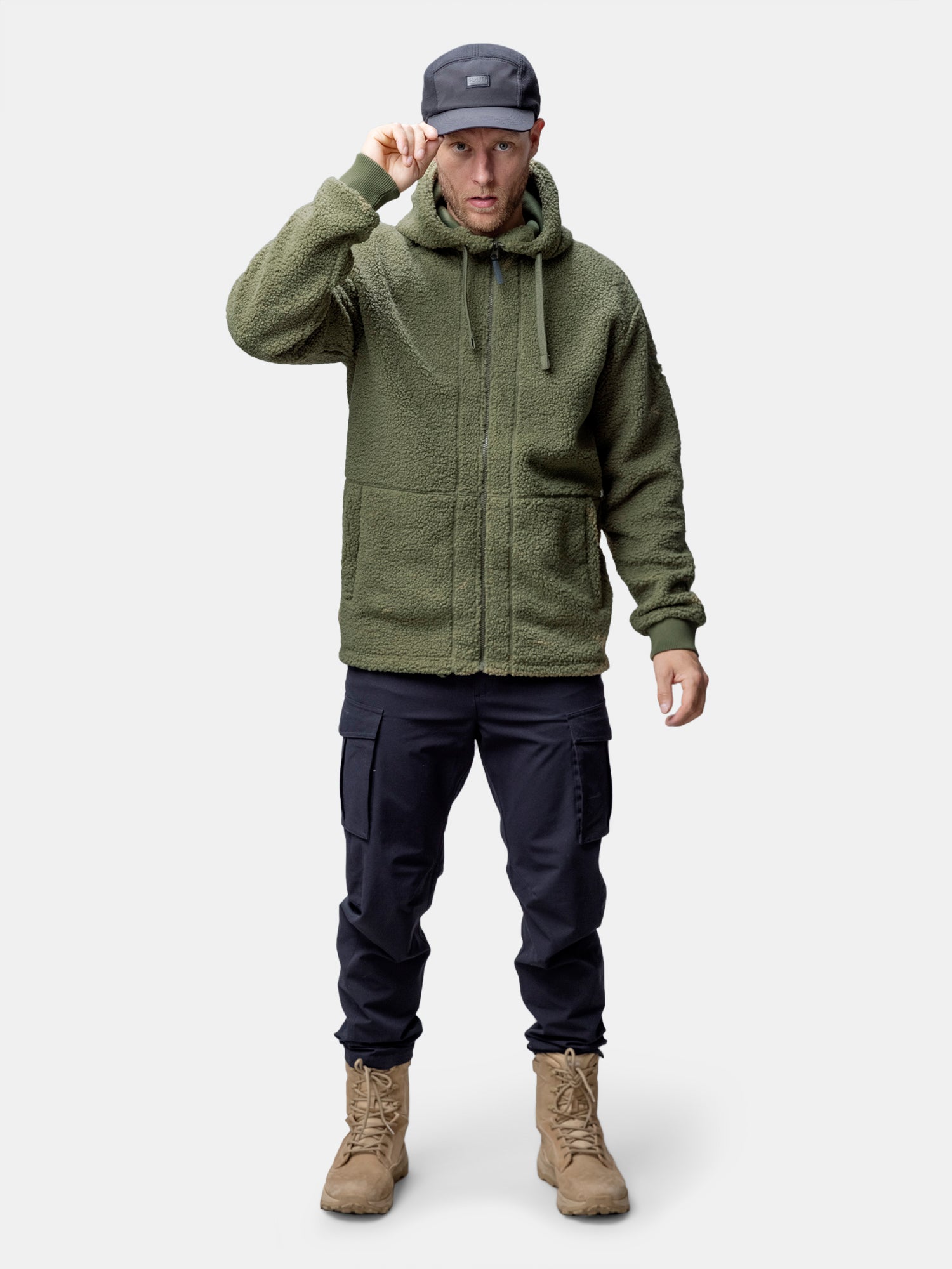 Ein Mann in einer Halti Lykky Fleece Jacke Herren, einer schwarzen Cargohose, hellbraunen Stiefeln und einer grauen Mütze steht mit dem Gesicht nach vorne.