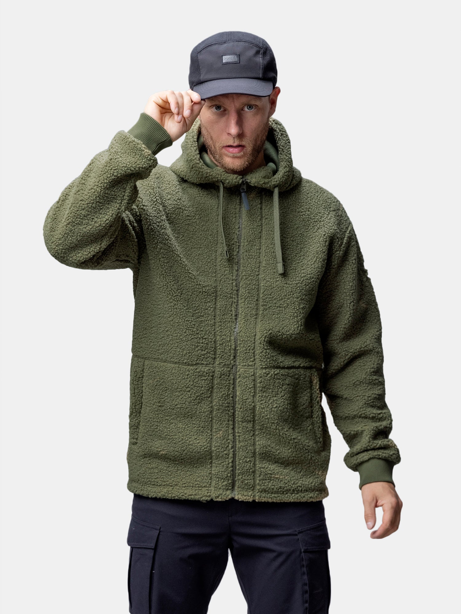 Eine Person in einer Halti Lykky Fleece Jacke Herren in Olivgrün und einer schwarzen Mütze, die in die Kamera schaut.