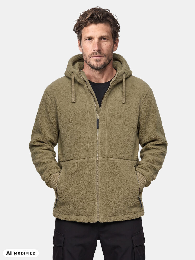 Ein Mann trägt eine Halti Lykky Fleece-Jacke für Herren in Olivgrün, steht mit dem Gesicht nach vorne und hat die Hände in den Taschen seines Kapuzenpullovers mit Reißverschluss.
