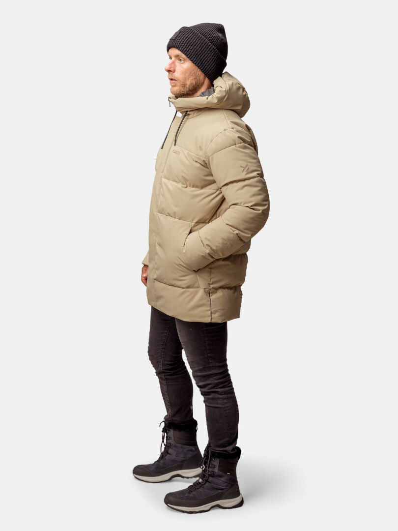 Ein Mann in einem Halti Sammal Isolationsparka Herren steht seitlich, die Hände in den Taschen, winterlich gekleidet.