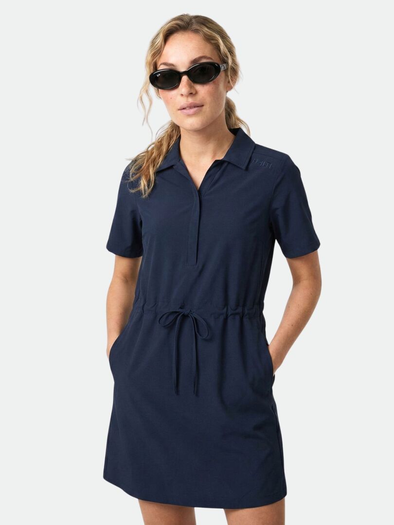 Frau in einem Halti Chipper II X-stretch Kleid mit Kordelzug in der Taille, UPF 50+, Hände in den Taschen und schwarzer Sonnenbrille.