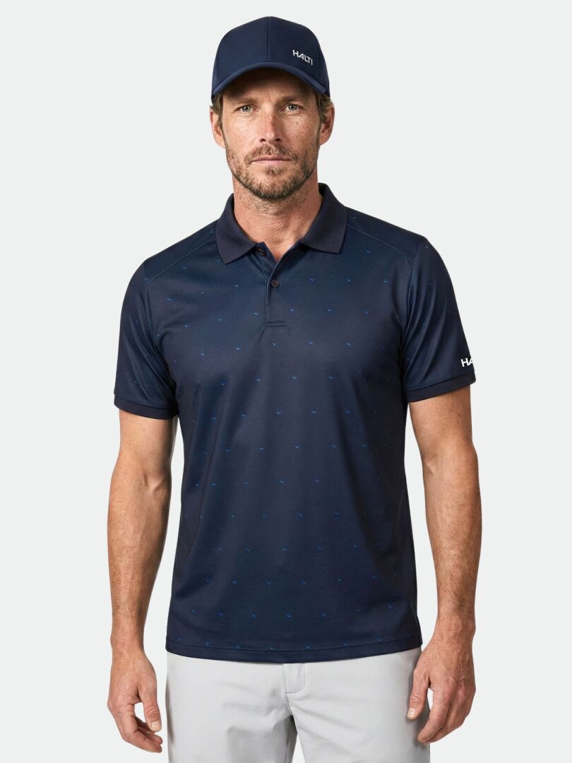 Mann in Halti Aridi Technisches Poloshirt Herren, passender Mütze und hellgrauer Hose, vor einfarbigem Hintergrund.