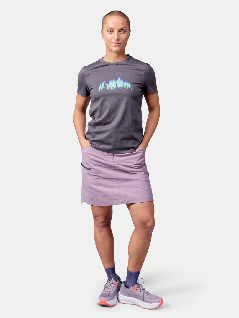 Person steht mit Händen in den Rocktaschen, trägt Halti Matka II T-Shirt Damen, lavendelfarbenen Rock und graue Turnschuhe.