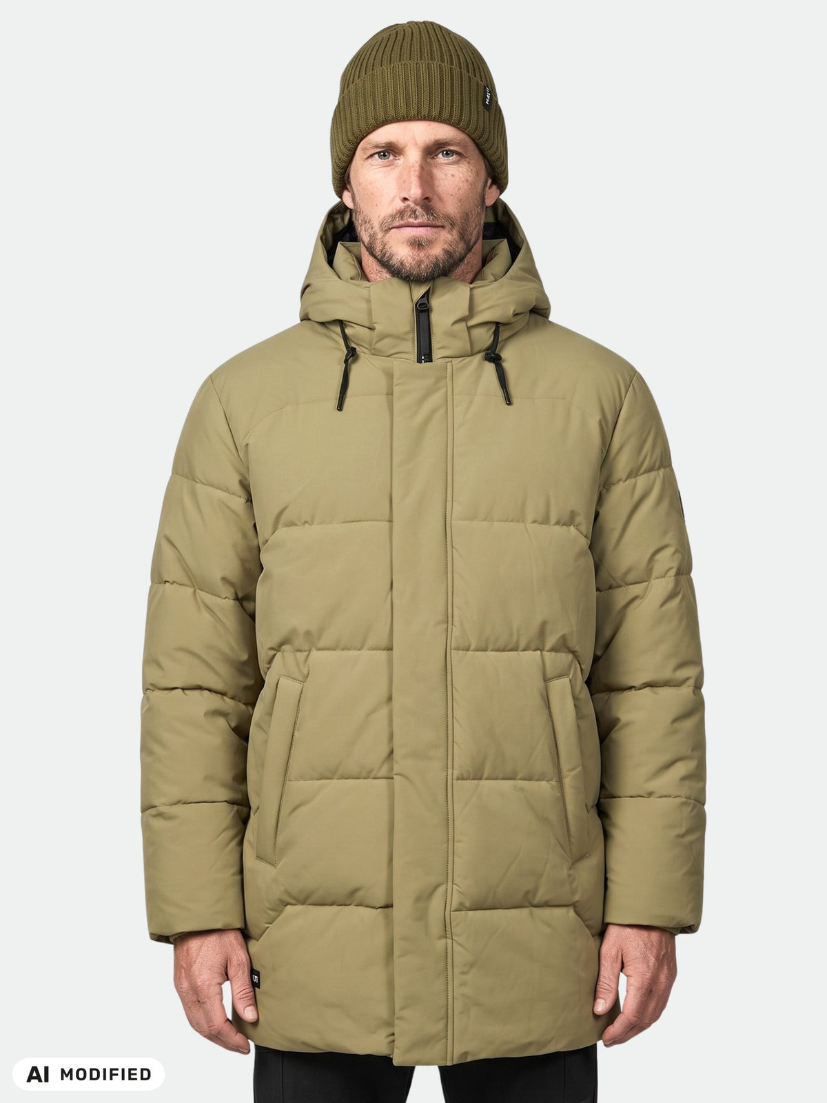 Ein Mann in einem grünen „Halti Brahe“-Daunenparka und einer Strickmütze steht mit dem Blick nach vorne vor einem hellen, einfarbigen Hintergrund.