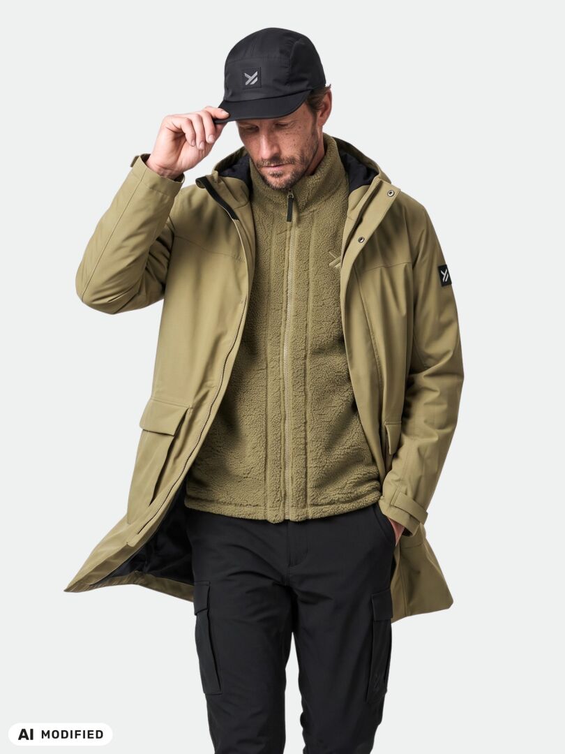 Ein Mann in einem „Halti Kortteli DX Insulated Parka“, einer Fleecejacke, einer schwarzen Hose und einer Mütze posiert mit der Hand an seiner Mütze.