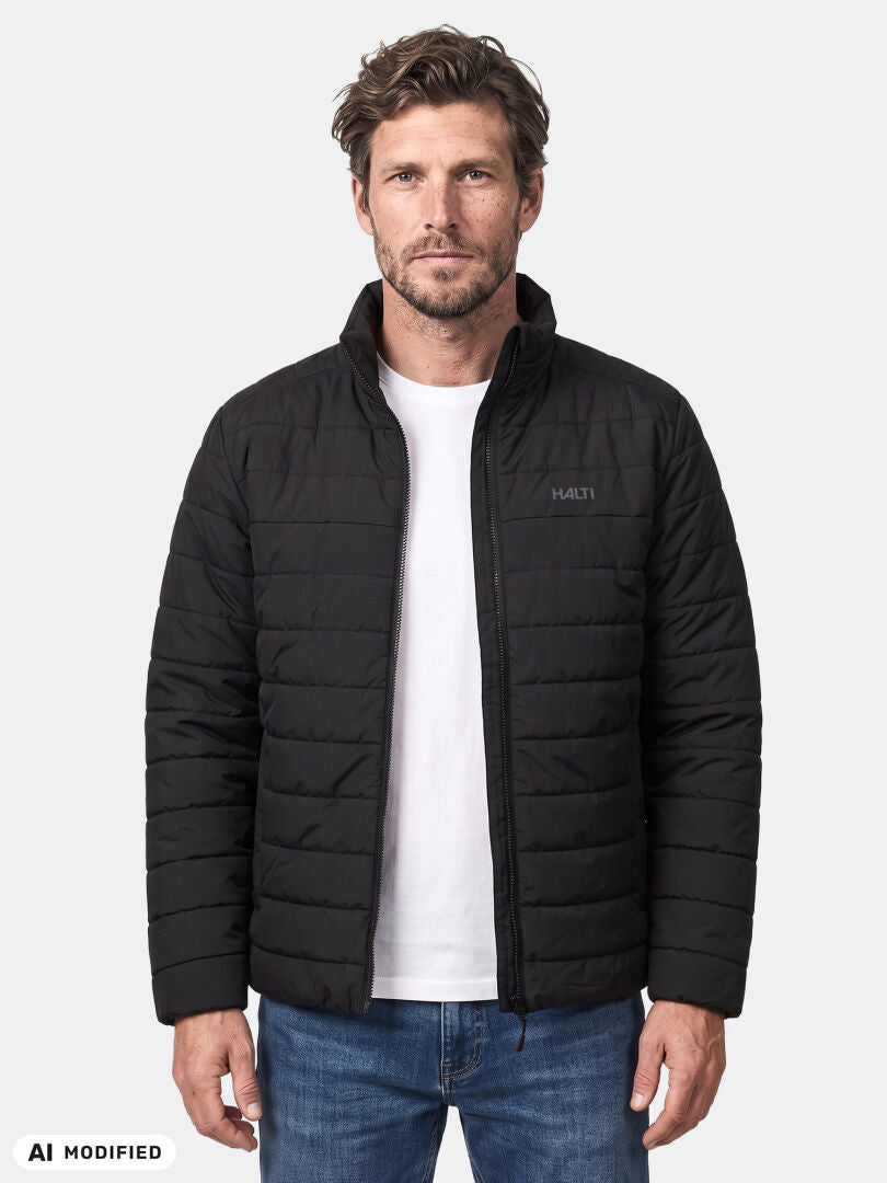 Ein Mann trägt die „Halti Rehia Gepolsterte Jacke Herren“ über einem weißen T-Shirt und blauen Jeans und steht vor einem schlichten, hellen Hintergrund.