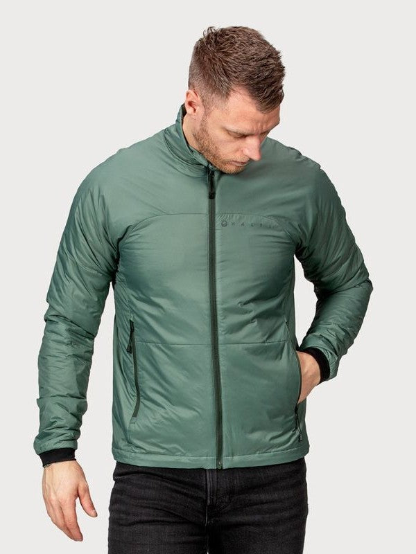 Ein Mann in grüner Halti Neon Primaloft Kunstfaserjacke Herren und schwarzer Hose steht mit einer Hand in der Tasche und schaut nach unten.