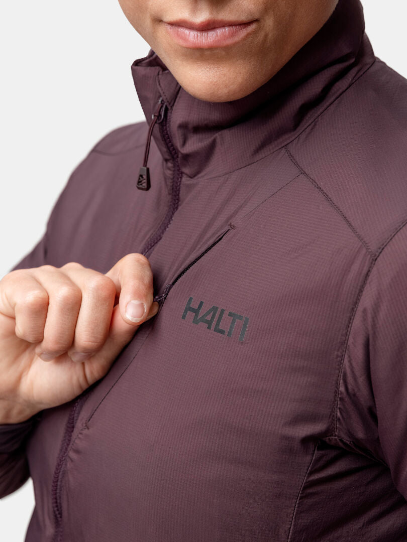 Eine Person in einer lila Halti Haave Insulation Primaloft Jacke Damen öffnet eine Brusttasche, das untere Gesicht ist sichtbar.