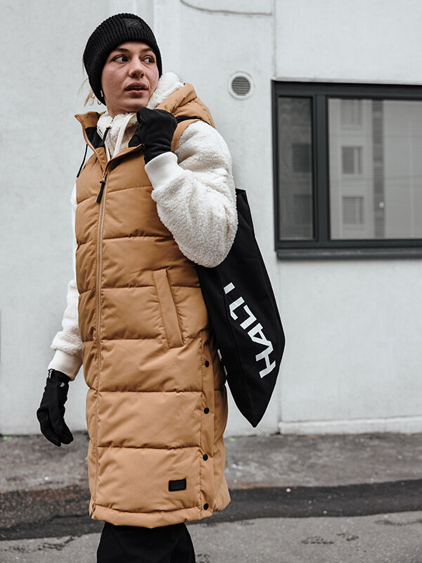 Eine Person mit hellbrauner Pufferweste und schwarzer Mütze trägt die Halti Viiri Fleece Handschuhe im Freien, um sich wohlig warm zu halten.