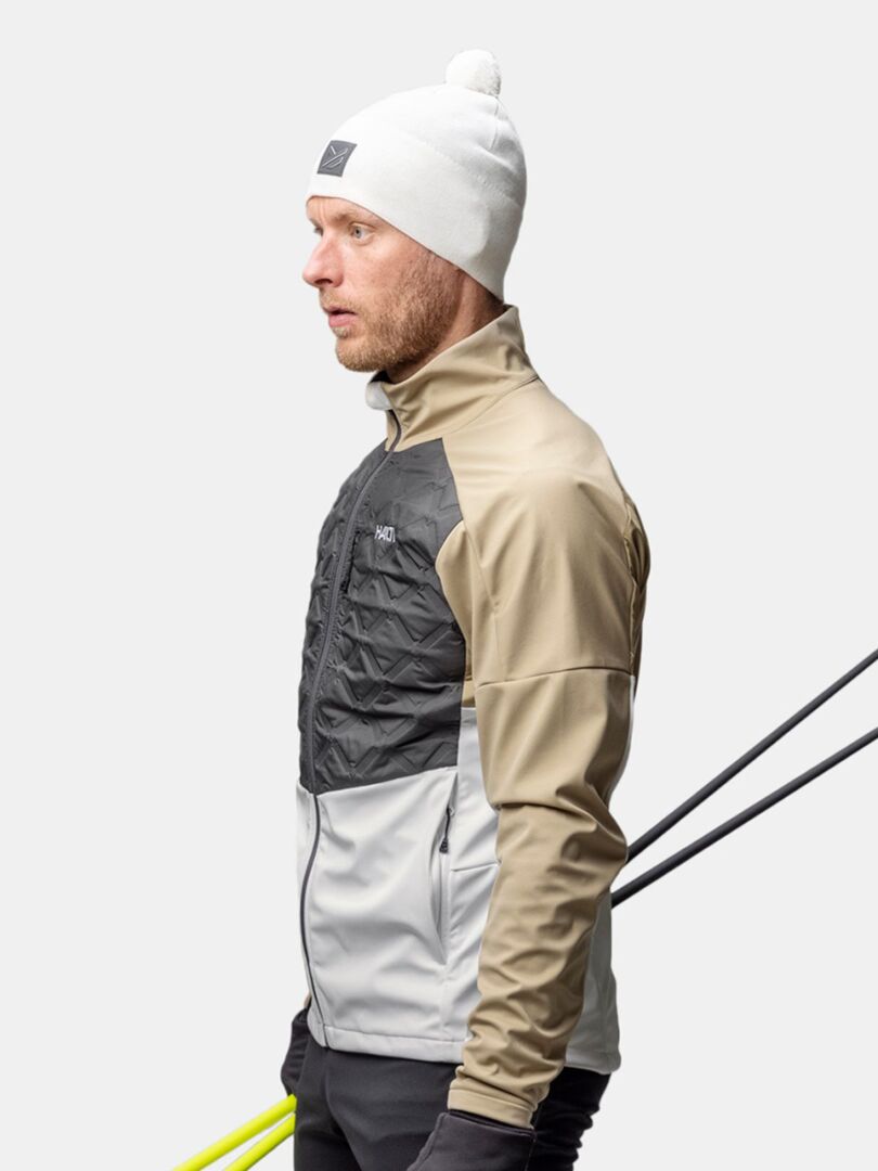 Ein Mann in einer Halti Pilke Mütze steht im Profil, die Skistöcke hinter sich haltend, bereit zum Skilanglauf.