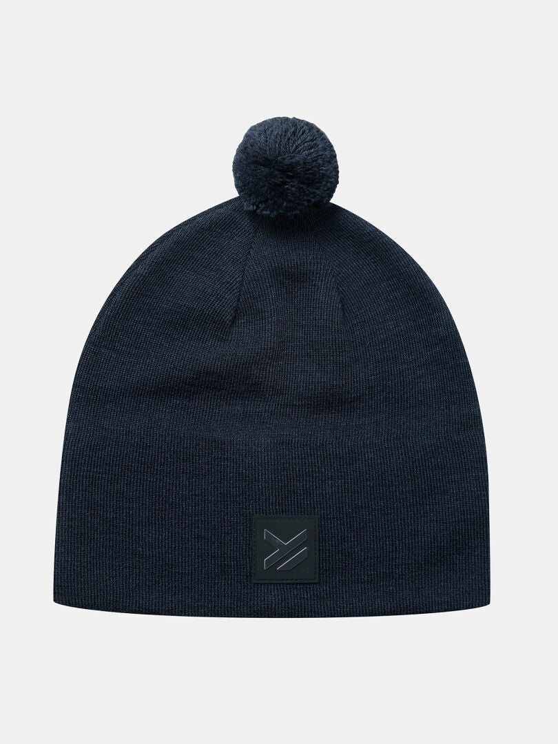 Halti Pilke Mütze: Marineblaue Mütze aus Merinowolle mit Bommel und schwarzem Aufnäher – ideal für Skilanglauf oder Wintersport.