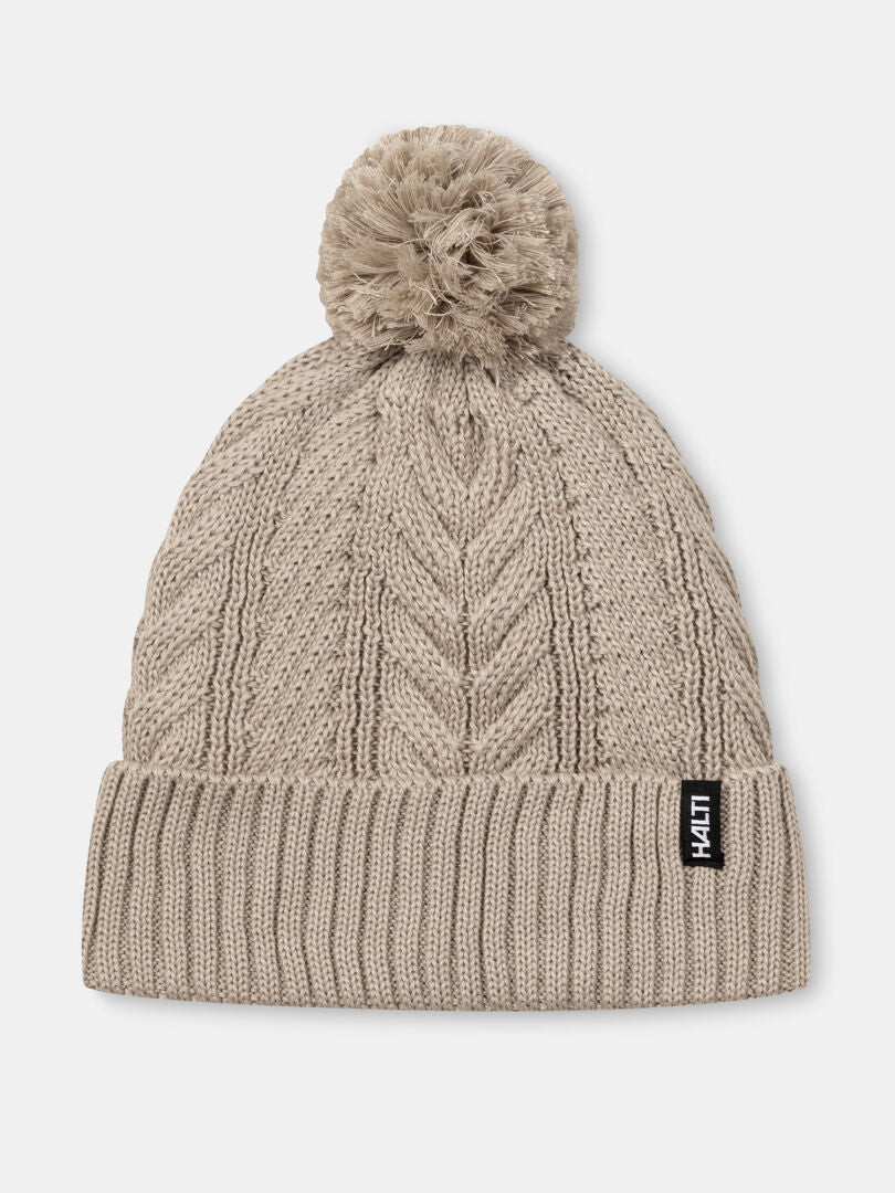 Hile Mütze von Halti: Beige, Zopfmuster, Fleecefutter, Pom-Pom und schwarzes Label auf dem Umschlag.
