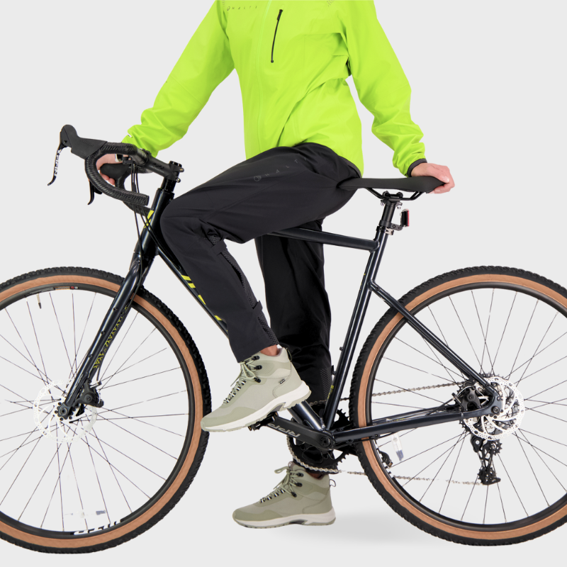 Die Person, die die Halti Liike Damen 3L DrymaxX Sporthose trägt, sitzt seitlich auf einem schwarzen Fahrrad mit hellbraunen Reifen vor einem schlichten Hintergrund.