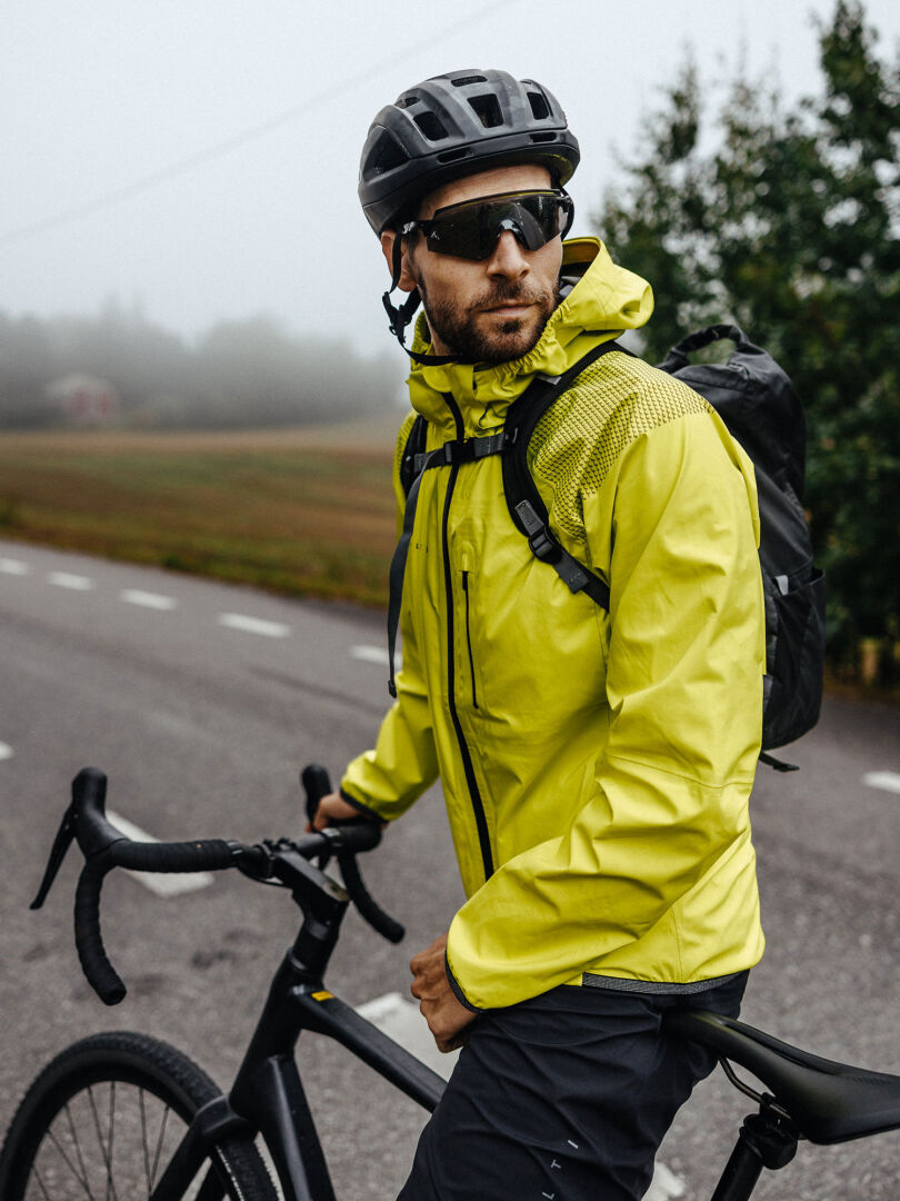 Ein Mann mit Helm und Sonnenbrille steht mit einer Halti Liike Herren 3L DrymaxX Sportjacke auf einer nebligen Straße neben seinem Fahrrad.