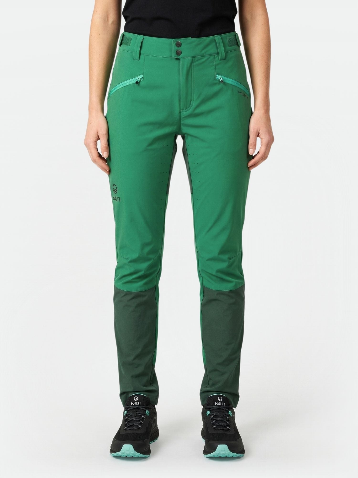 Frau in grüner Halti Tracks Damen X-stretch Hose, schwarzem Shirt und Turnschuhen, stehend mit Blick nach vorne.