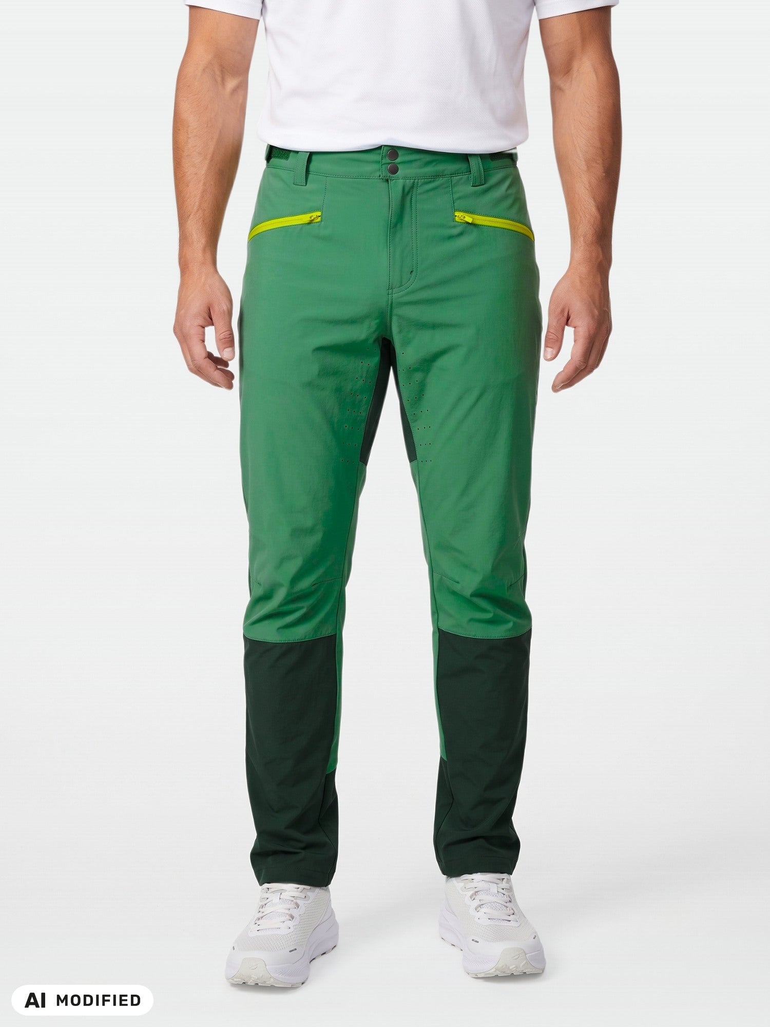 Eine Person trägt eine „Halti Tracks Herren X-Stretch“-Hose mit grünen Knien und gelben Reißverschlüssen, ein weißes Hemd und weiße Turnschuhe.