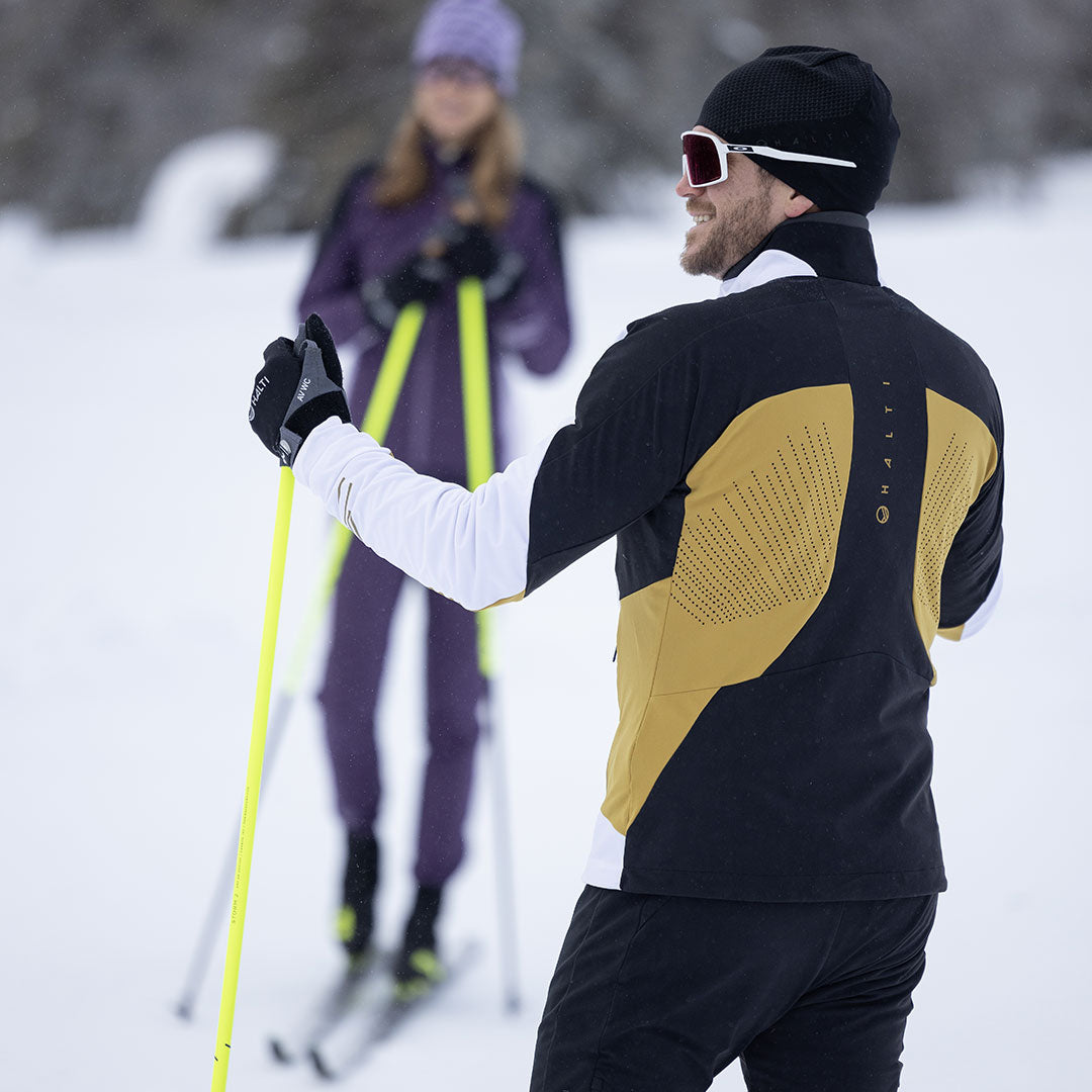 Zwei Personen in Wintersportkleidung, eine davon trägt die Halti Veloce Langlaufjacke Herren, beim Langlaufen auf Schnee.