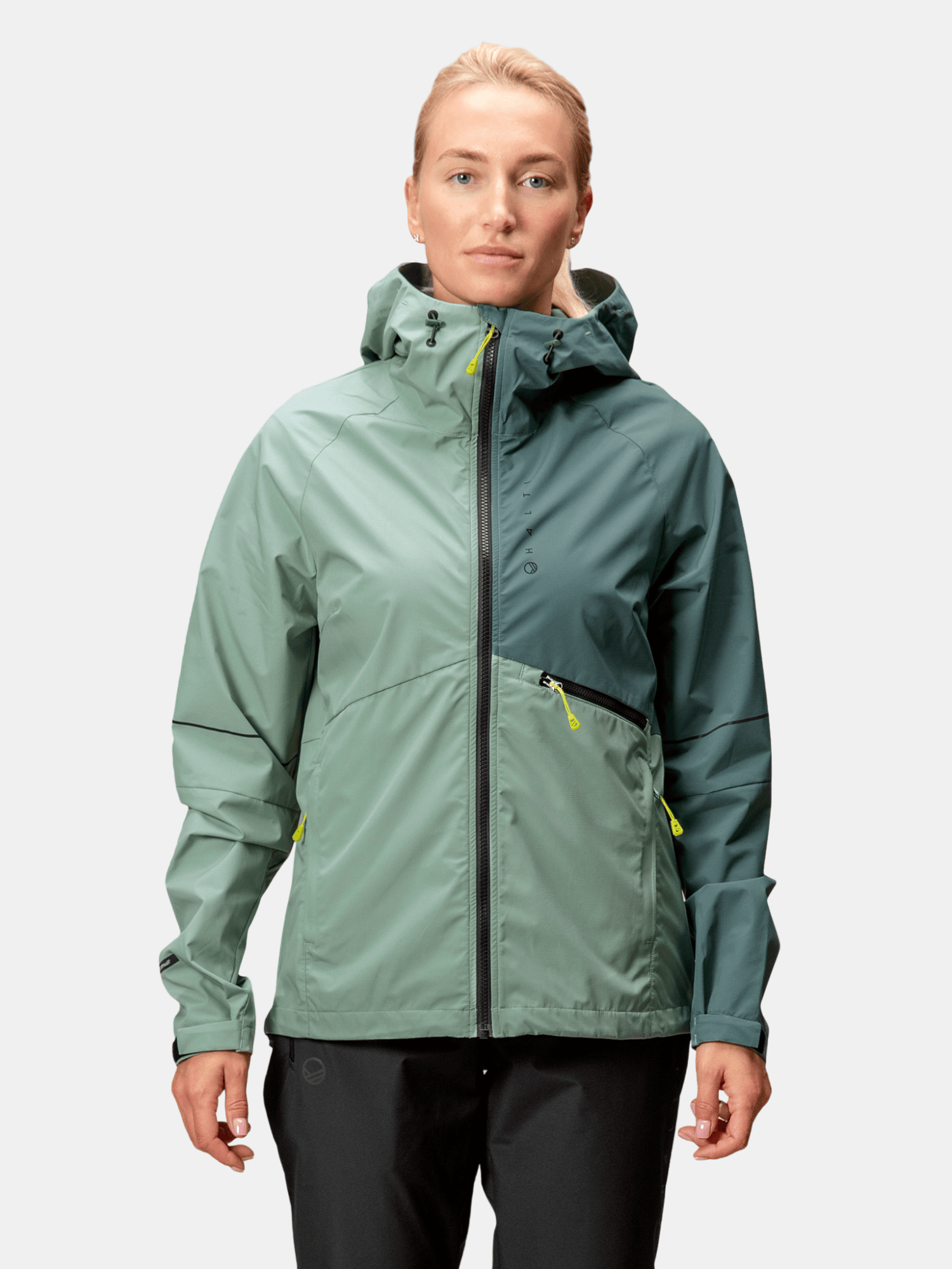Eine Frau trägt die Halti Shelter Stormwall 3L Jacke vor einem hellgrauen Hintergrund.