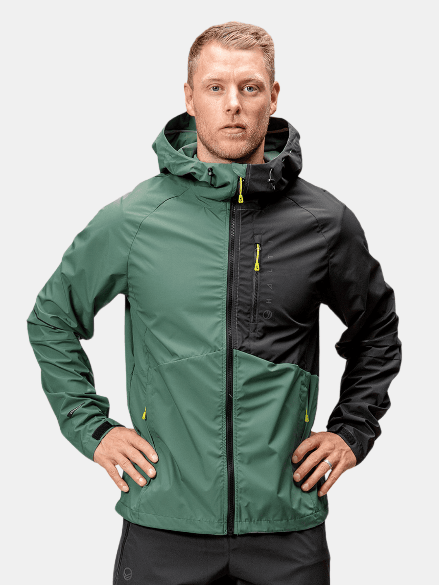 Ein Mann in einer grün-schwarzen Halti Shelter Stormwall 3L Jacke für Herren steht mit dem Gesicht nach vorne und den Händen in den Hüften.
