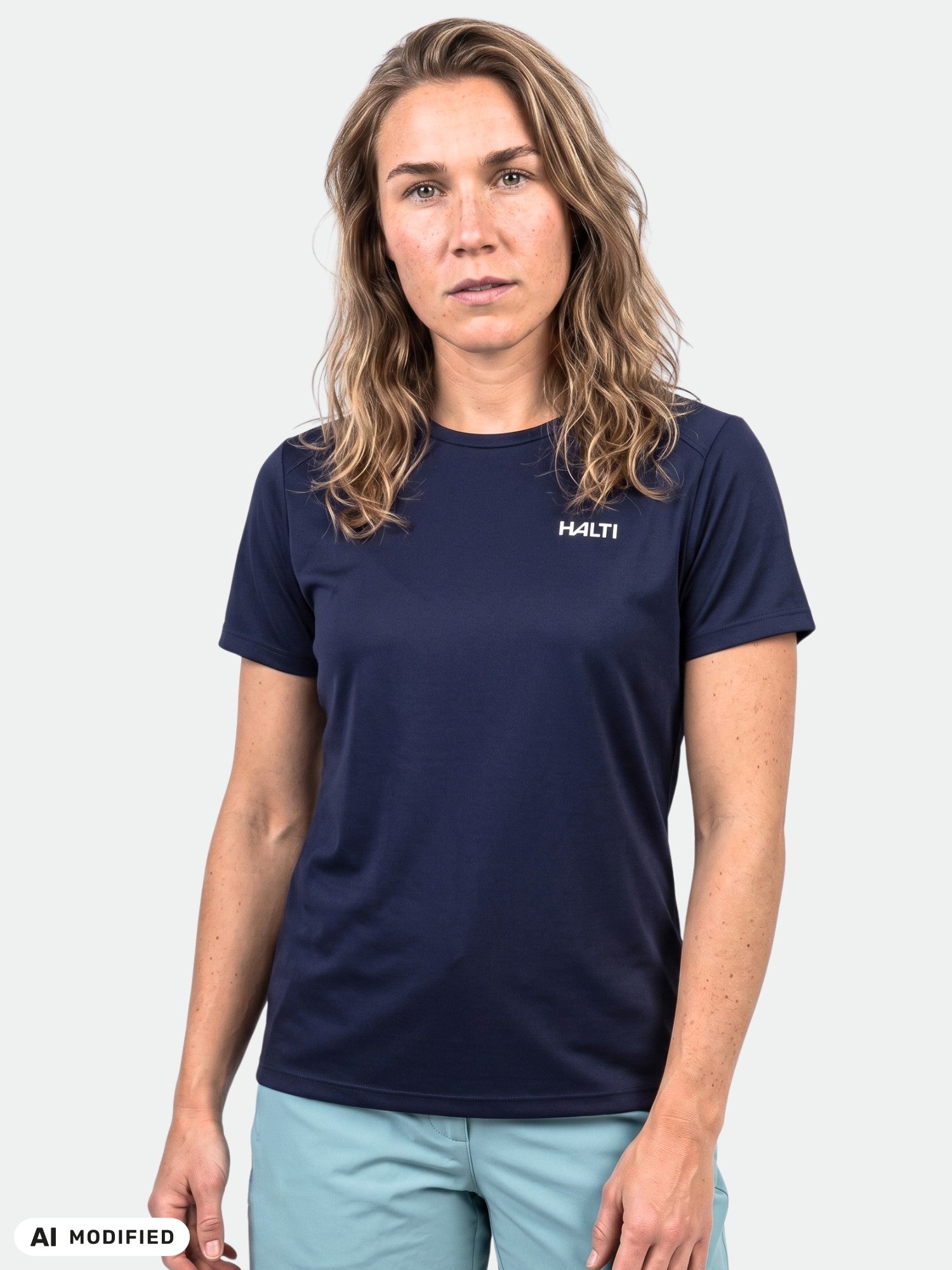 Eine Frau mit gewelltem Haar trägt ein „Halti Salves“-T-Shirt für Damen in Marineblau und hellblaue Shorts vor einem einfarbigen Hintergrund.