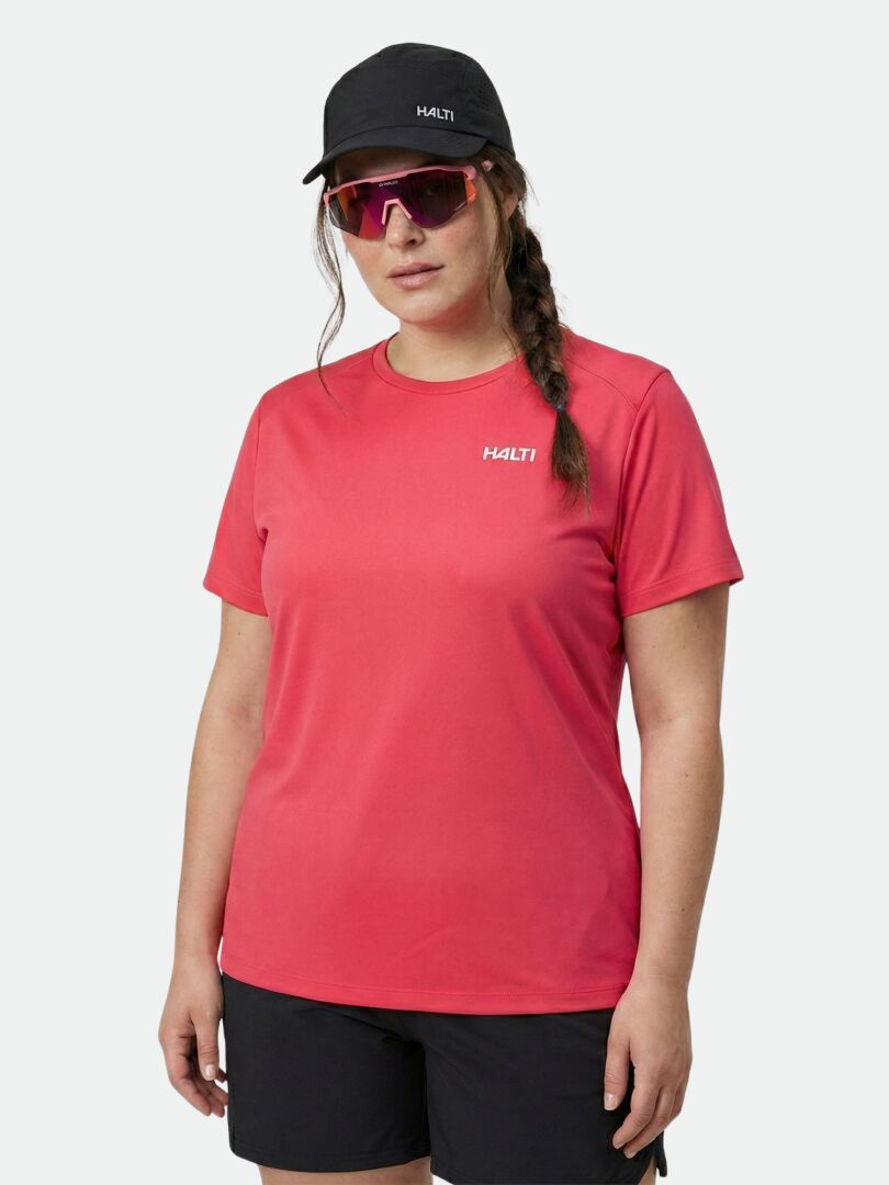 Frau in Halti Salves T-Shirt Damen Plus, schwarzen Shorts, Mütze und rosa Sonnenbrille vor hellem Hintergrund.
