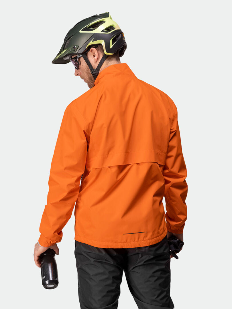 Eine Person mit schwarzem Helm und orangefarbener Halti Triant DX Radjacke für Herren blickt abgewandt und hält in der rechten Hand eine Wasserflasche.