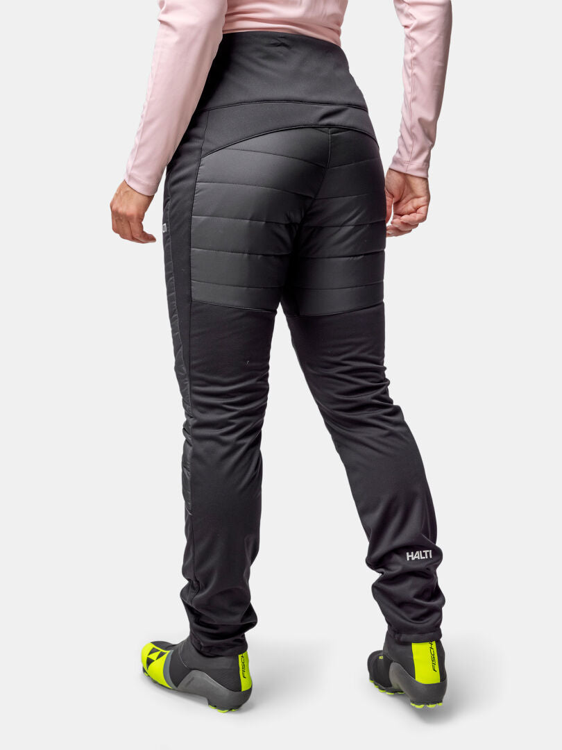 Person in Halti Hanki 2 Hybrid Langlaufhose Damen, einem hellrosa langärmeligen Oberteil und neongelben Fahrradschuhen, von hinten gesehen.