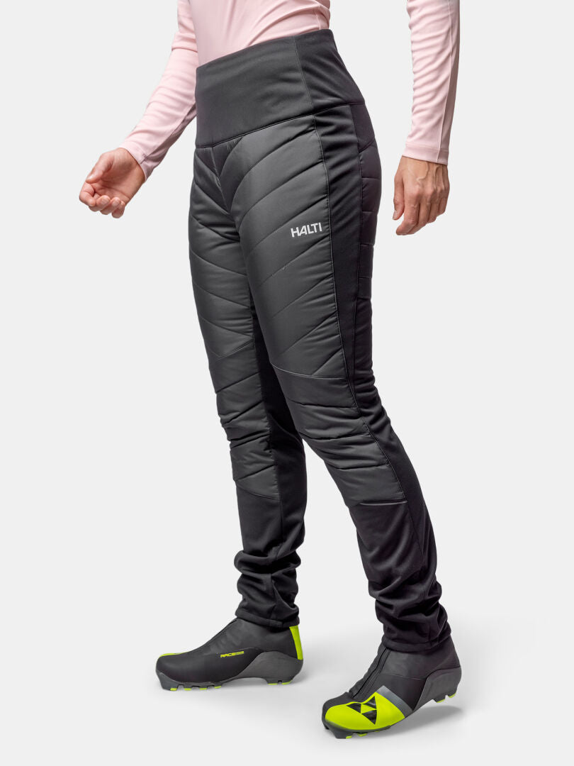 Frau in schwarzer Halti Hanki 2 Hybrid Langlaufhose, gelben Turnschuhen und rosa Oberteil - ideal für Winteraktivitäten.