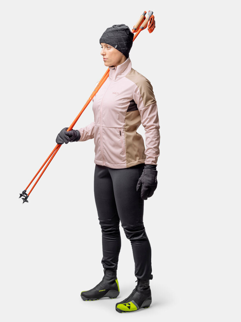 Frau in Wintersportkleidung hält orangefarbene Skistöcke, bereit zum Wintertraining im Halti Huuru Langlaufanzug Damen.