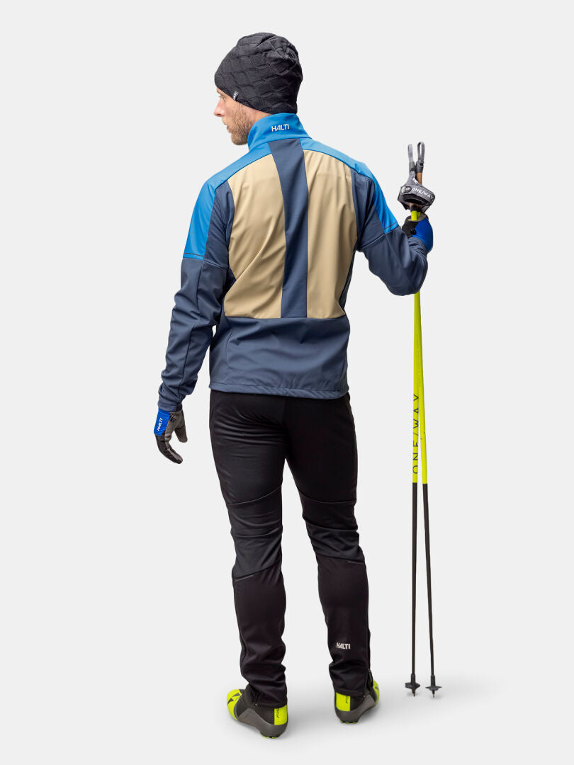 Ein Mann in der Halti Framover Langlaufjacke Herren schaut weg, hält Skistöcke und macht ein Friedenszeichen.