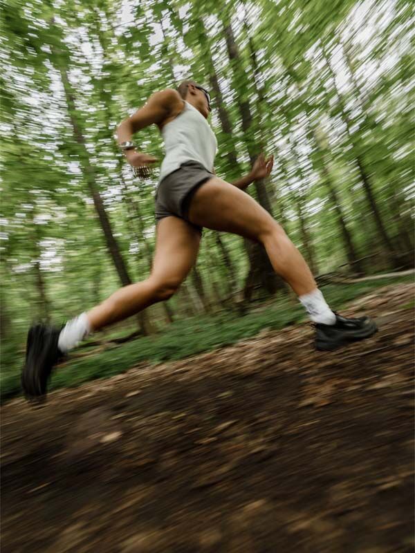 In Halti Uurto Shorts Damen rennt eine Läuferin einen Waldweg hinunter, und die verschwommenen Bäume zeigen ihr schnelles Tempo.