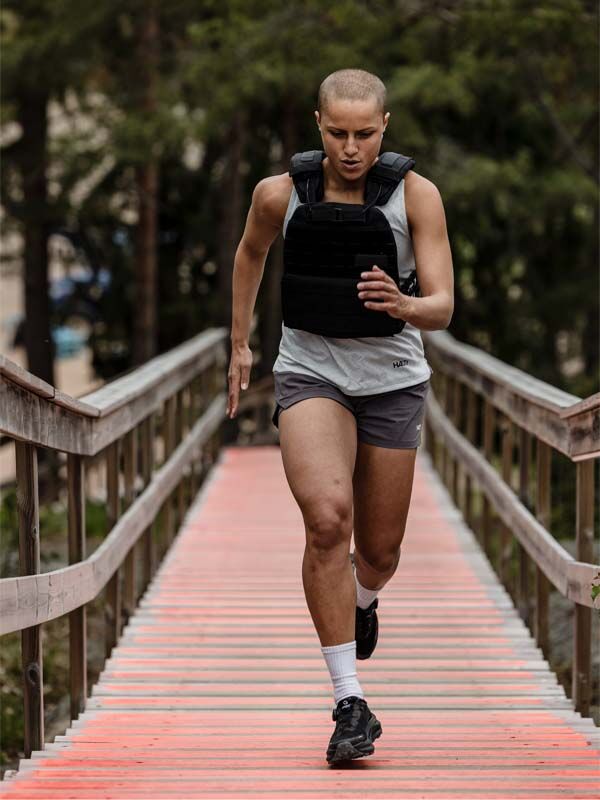 Eine Person läuft in einem Halti Oulanka T-Shirt Damen, einer Gewichtsweste, Shorts und schwarzen Laufschuhen eine rote Außentreppe hinauf.