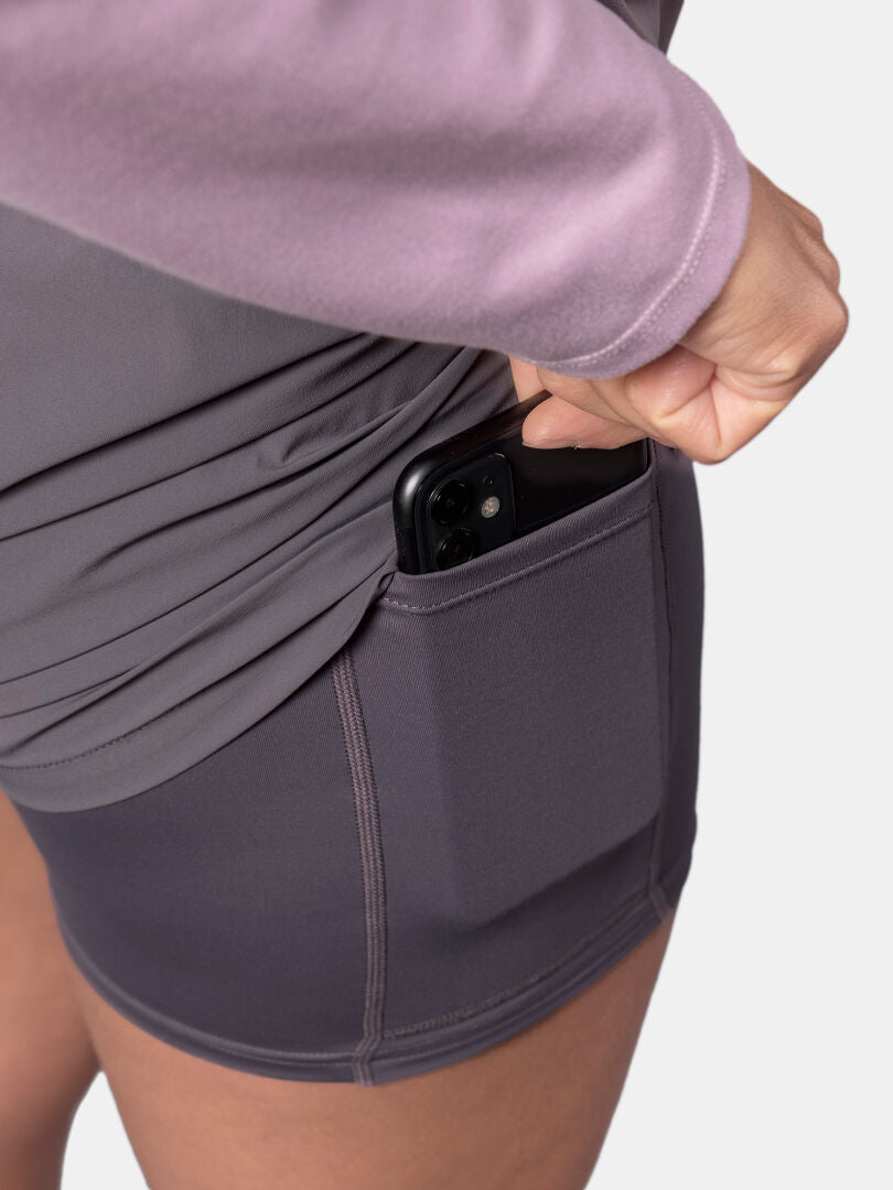 Ein schwarzes Smartphone in Halti Uurto Shorts Damen, feuchtigkeitsableitend, mit einem malvenfarbenen Oberteil.