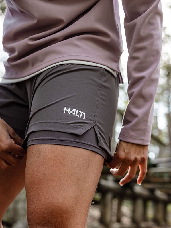 Person in Halti Uurto Shorts Damen und lilafarbenem langärmeligem Hemd, die Shorts im Freien anpassend.