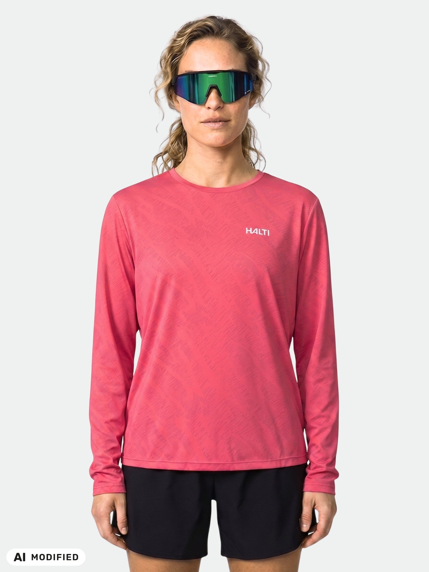 Frau in einem rosa Halti Oulanka Trainingsshirt für Damen mit UPF 50+ und schwarzen Shorts, die eine reflektierende Sonnenbrille trägt.