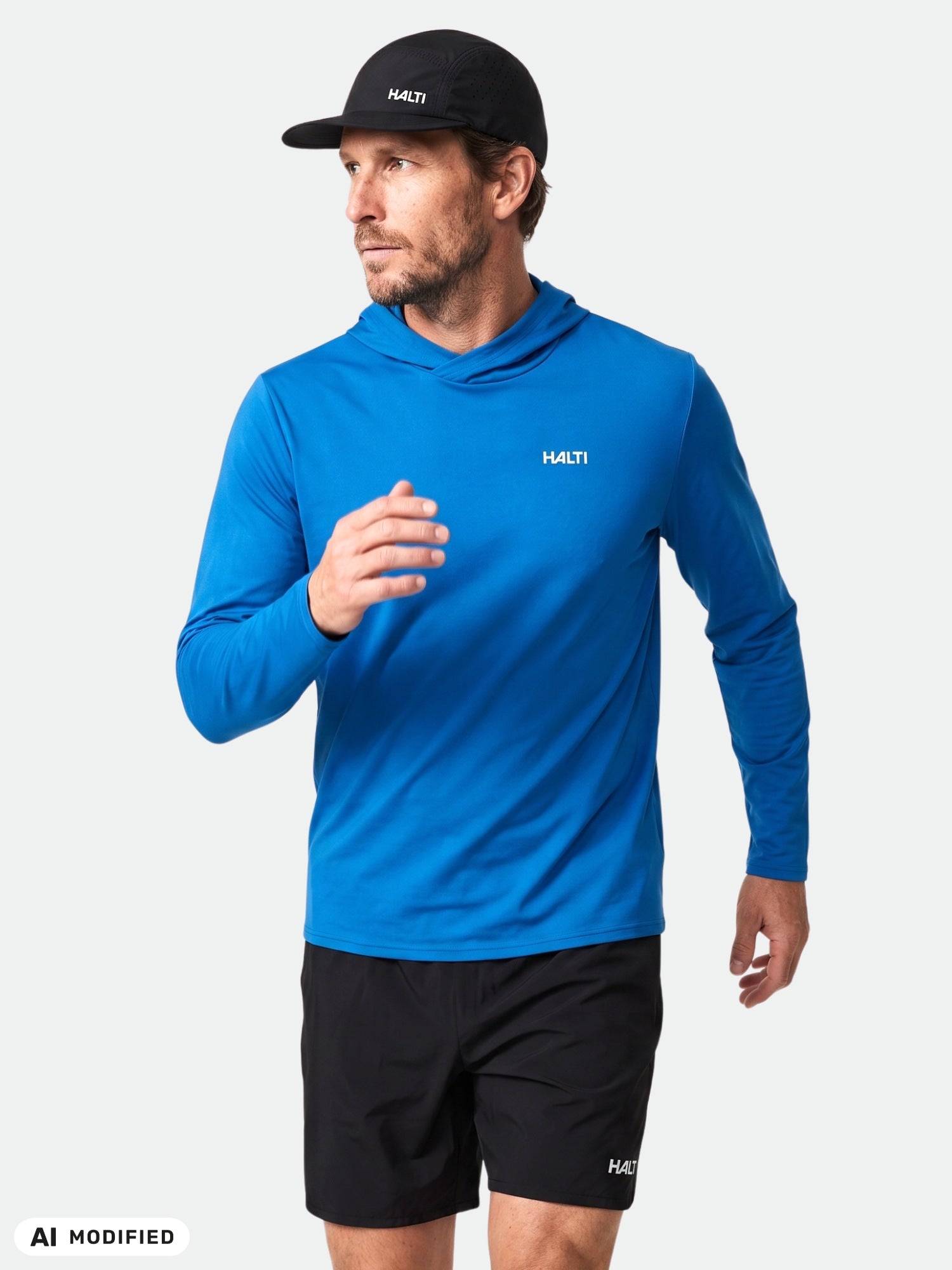 Ein Mann in einem „Halti Kaltio“-Trainingshoodie für Herren, schwarzen Shorts und einer Kappe posiert vor einem schlichten weißen Hintergrund.