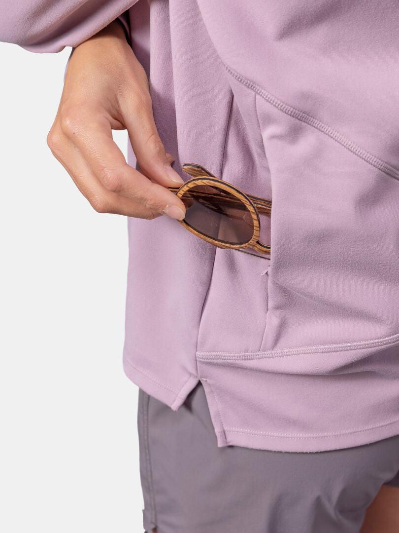 Eine Person in einer hellvioletten Halti Kaltio Trainingshoodie Damen steckt eine Holzsonnenbrille in eine Seitentasche.