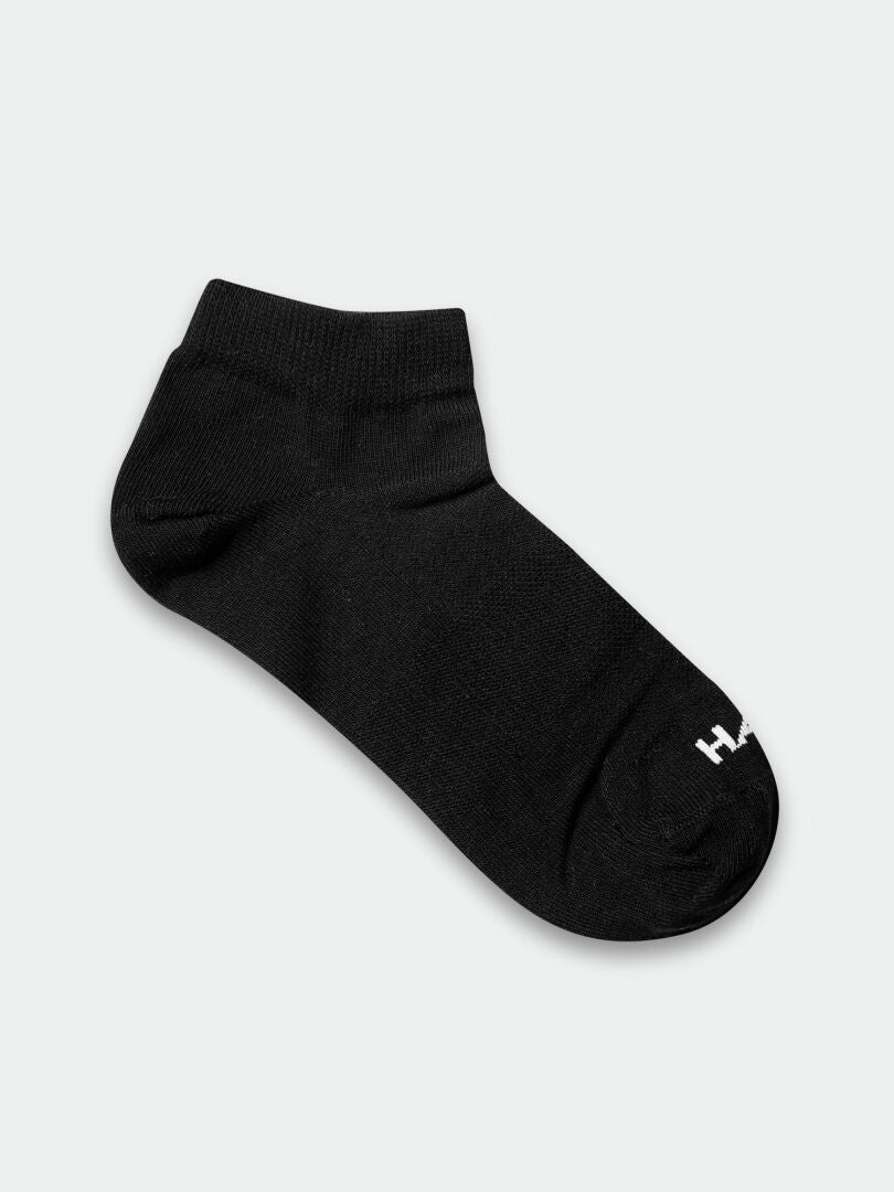 Eine einzelne schwarze Halti Outdoor Sport Low Socke mit einem kleinen weißen Logo in der Nähe der Zehenpartie, abgebildet auf einem schlichten hellen Hintergrund.
